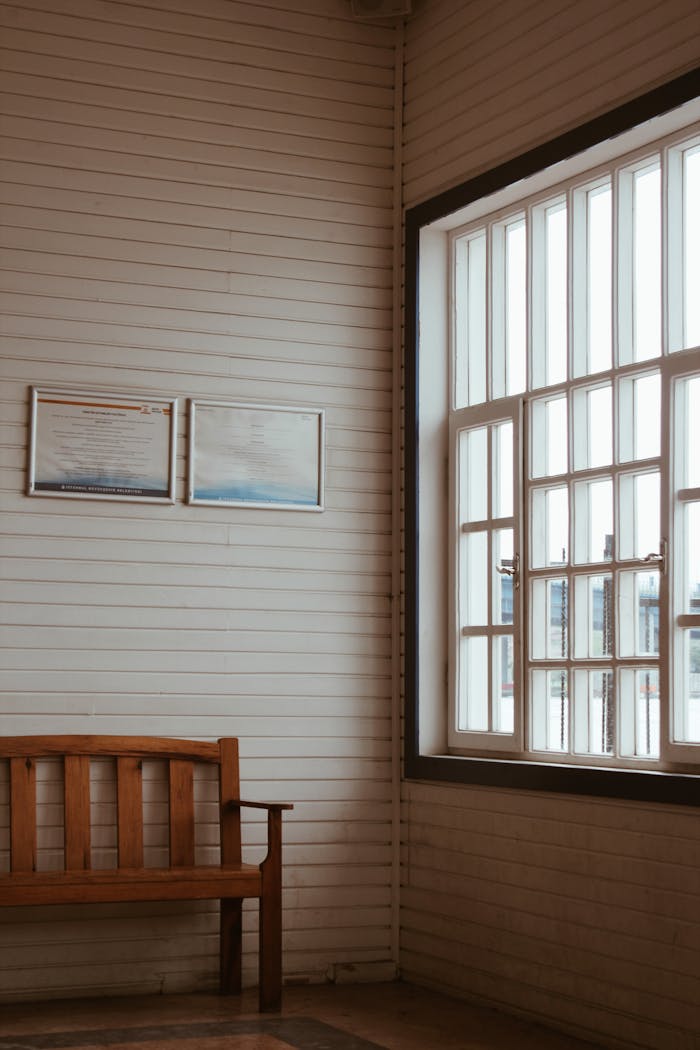 Warm indoor scene with a wooden bench by a large sunlit window in a rustic setting.