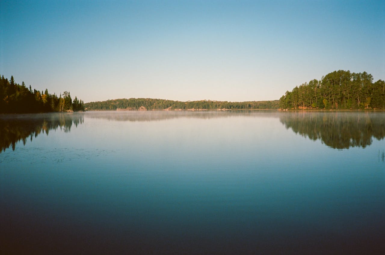 Tranquil lake reflecting lush forests, captured at sunrise, creating a serene and peaceful atmosphere.